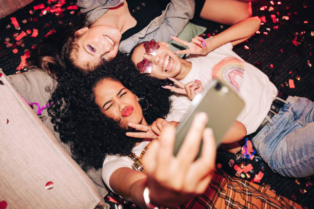 Capturing crazy party moments Capturing crazy party moments. Top view of three happy friends taking a selfie while lying on the floor at a house party. Group of cheerful female friends having fun together on the weekend. women selfies stock pictures, royalty-free photos & images