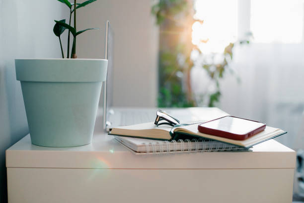 istock White desk table with notebook, phone, eyeglasses, home plant. 1397869325