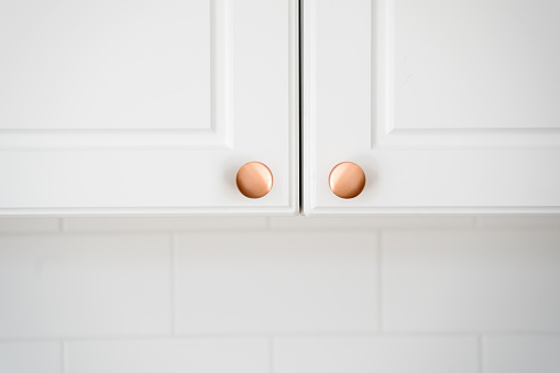 Two small round copper door knob on white kitchen cabinet