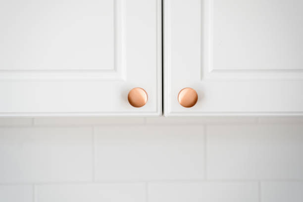 Two small round copper door knob on white kitchen cabinet Concept of replacement or install of new handle on furniture in classic style. Close up view of two small round copper door knob on white kitchen cabinet over copy space tiled wall knob stock pictures, royalty-free photos & images