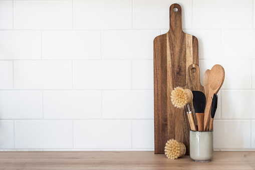 Wooden cutting board and dishwashing brushes on table in kitchen. Home comfort concept. Eco-friendly kitchenware idea. Cooking at home. Household equipment