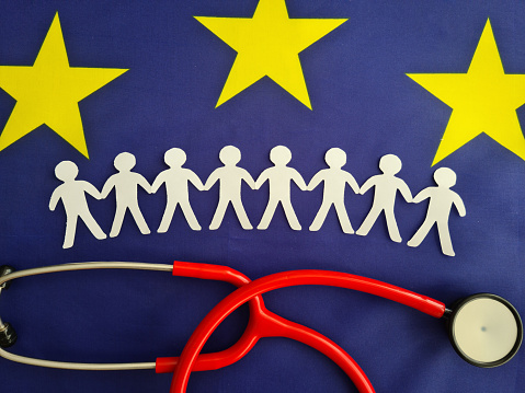 Stethoscope with the flag of European Union and figurines of people hold hands from paper