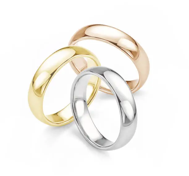 Three plain gold wedding rings in rose gold, white gold and yellow gold grouped together and isolated on white background.