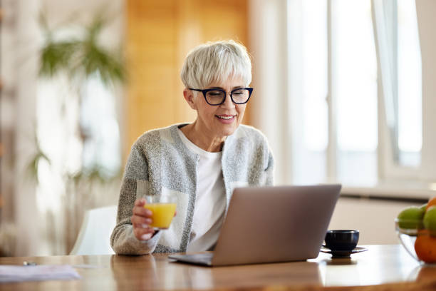istock Happy senior woman drinking juice while using laptop at home. 1397873862