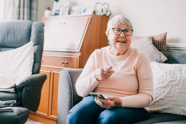 Portrait of happy laughing senior woman using phone while sitting onon the sofa at home. Mature older lady is excited to receive good news via smartphone. Seniors and technology. Selective focus retrato de una mujer mayor feliz y risueña usando el teléfono mientras está sentada en el sofá de casa. la anciana madura está emocionada de recibir buenas noticias a través de un teléfono inteligente. personas mayores y tecnología. enfoque selecti
