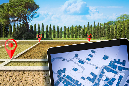 Land plot management - real estate concept with a vacant land on a plowed agricultural field available for building construction and digital tablet with imaginary cadastral map