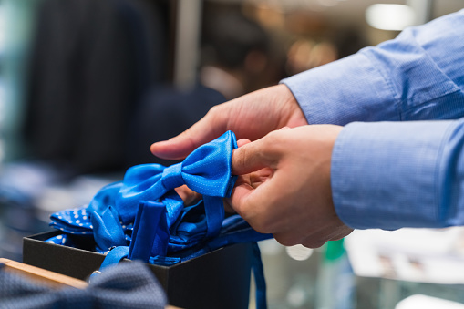 Cropped hands of young male owner examining blue bow tie at clothing boutique