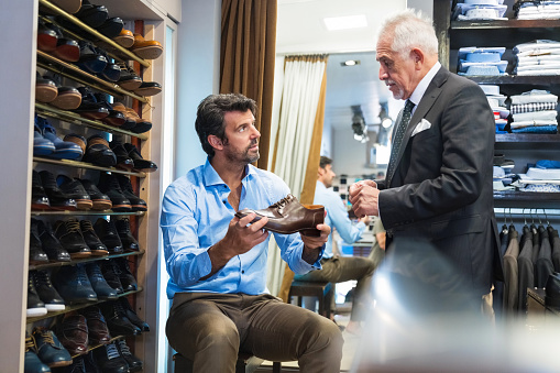Mature customer discussing over shoe with senior male menswear showroom owner