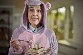 Senior woman in unicorn costume eating a cake at home.