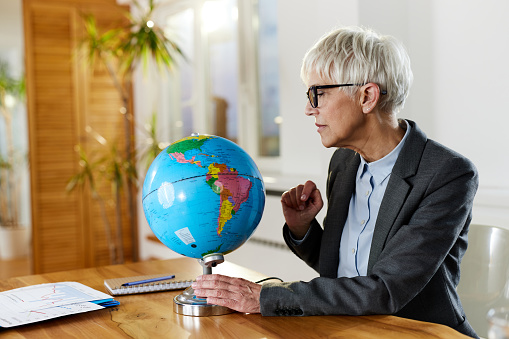 Mature female entrepreneur examining the globe while working in the office.