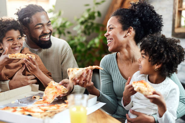 szczęśliwa czarna rodzina rozmawiająca podczas jedzenia pizzy na lunch w jadalni. - pizza eating african descent lunch zdjęcia i obrazy z banku zdjęć