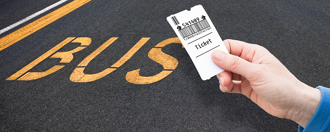 Bus text written in yellow on a dark asphalt with a female hand holding a bus ticket - Travel by bus concept image - meaningless, totally invented QR code