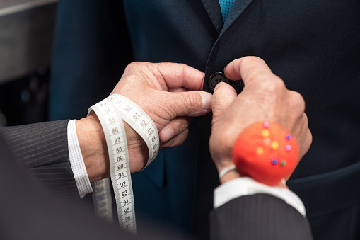 Hands of senior male tailor buttoning suit for customer at clothing store