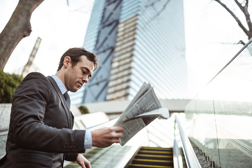 African businessman wearing suit and tie sitting at coffee shop and reading daily newspaper.