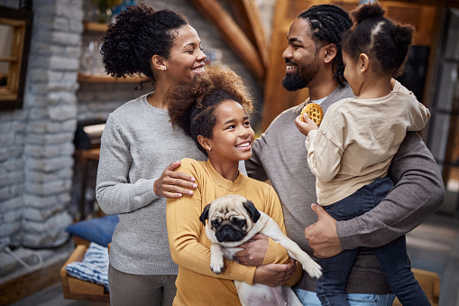 Happy black parents with their small girls and a dog communicating while spending time at home.