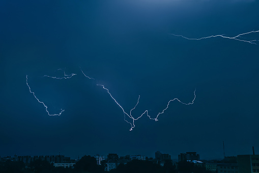 Lightning in sky over city. Bright flashes on dark night. Thunderclouds and electricity discharges in  atmosphere. Night cityscape.