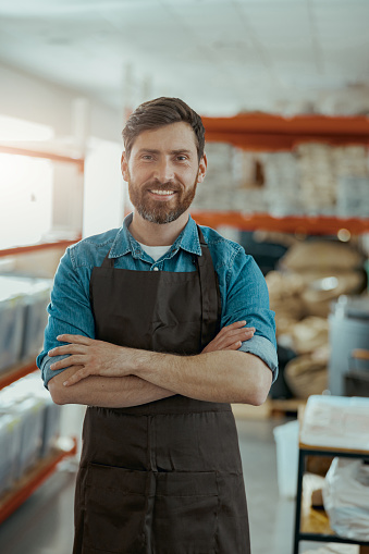 Smiling business owner in uniform standing on the background of own coffee roasting factory