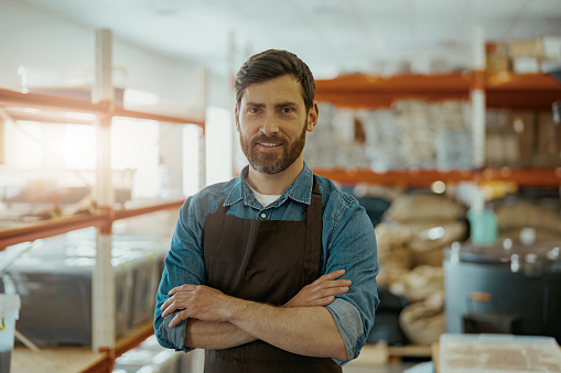 Portrait of smiling business owner on background of warehouse in small coffee factory looking camera