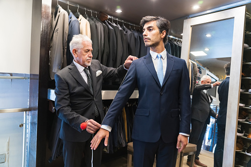 Senior male tailor measuring sleeve of customer with tape at clothing store