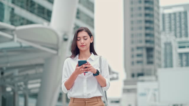 Businesswoman using phone and walking to work in modern city