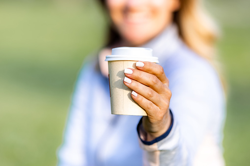 Close-up of a woman holding disposable coffee cup in nature