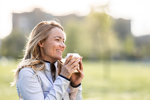 Smiling woman holding disposable coffee cup in nature