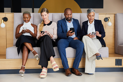 istock Diverse businesspeople using smart phones on a bench in an office lounge 1397881846