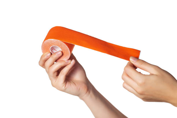 the girl holds in her hands on a white background a kinesiological tape of orange color, isolate. taping muscles and joints, close-up - kinesio imagens e fotografias de stock