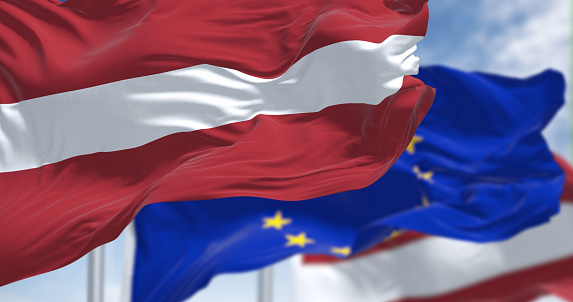 Detail of the national flag of Latvia waving in the wind with blurred european union flag in the background