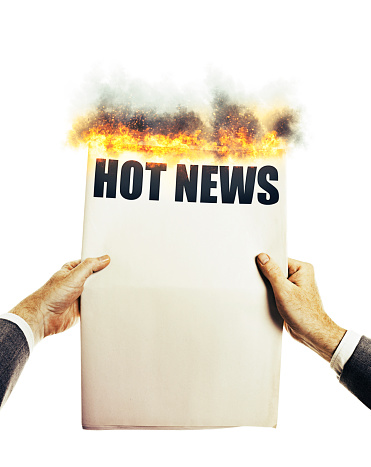 Flames erupt from the top of a newspaper held by a well-dressed man's hands.