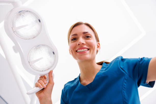 Female dentist adjusting light above dental chair stock photo