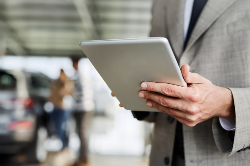 Close up of unrecognizable manager working on touchpad in a car showroom.