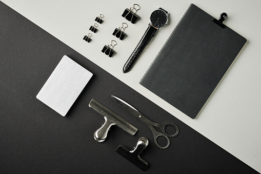 Overview of black clipboard, wristwatch, set of clips, scissors and white notepad on contrast background or workplace of business person