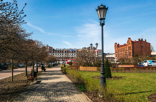 A brick walkway in East Boston's Pier's Park invites you to stroll past the lush green grass and bright flowers to the black wrought-iron railing by the waterfront. Gaze out across the Boston Harbor to see sailboats gliding by or the numerous buildings of all sizes in downtown Boston. With the clear blue sky, lights are not needed, but decorative street lamps are ready for nightfall. HDR Image.