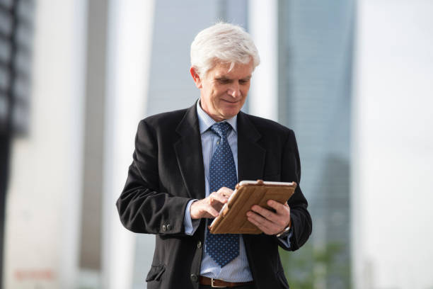 istock senior grey-haired businessman using a tablet, standing in front of an office building. old business man concept. 1397890755