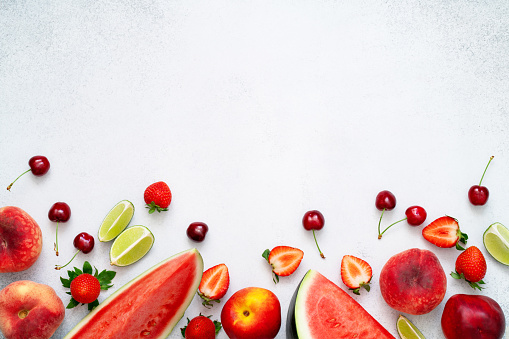 Watermelon, peach, strawberry, lime, cherry and nectarine on grey background. Slices of fresh red fruits and berries. Healthy summer diet with vitamins and antioxidants. Copy space, top view, flat lay.