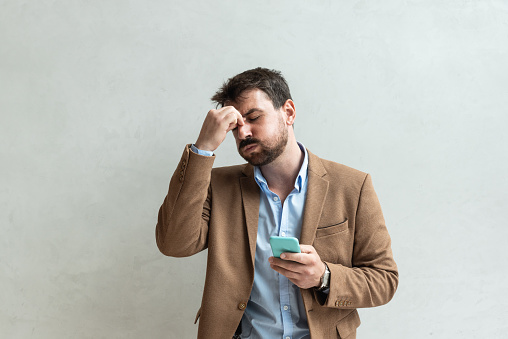 Young successful business man stressed after reading negative text message on his smartphone. Businessperson got headache when his offer is not accepted by company.