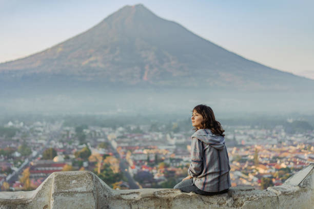 женщина сидит на фоне вулкана в гватемале - volcano erupting lava fire стоковые фото и изображения