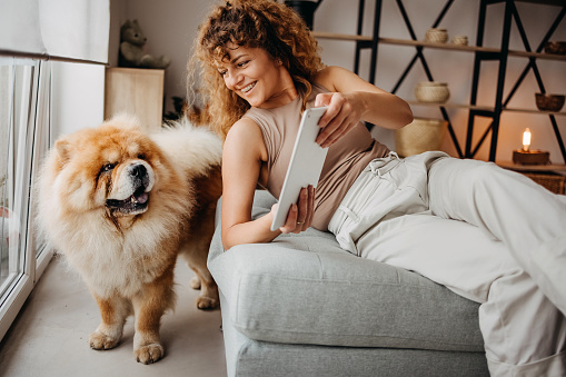 Woman on a stool uses a tablet with her dog