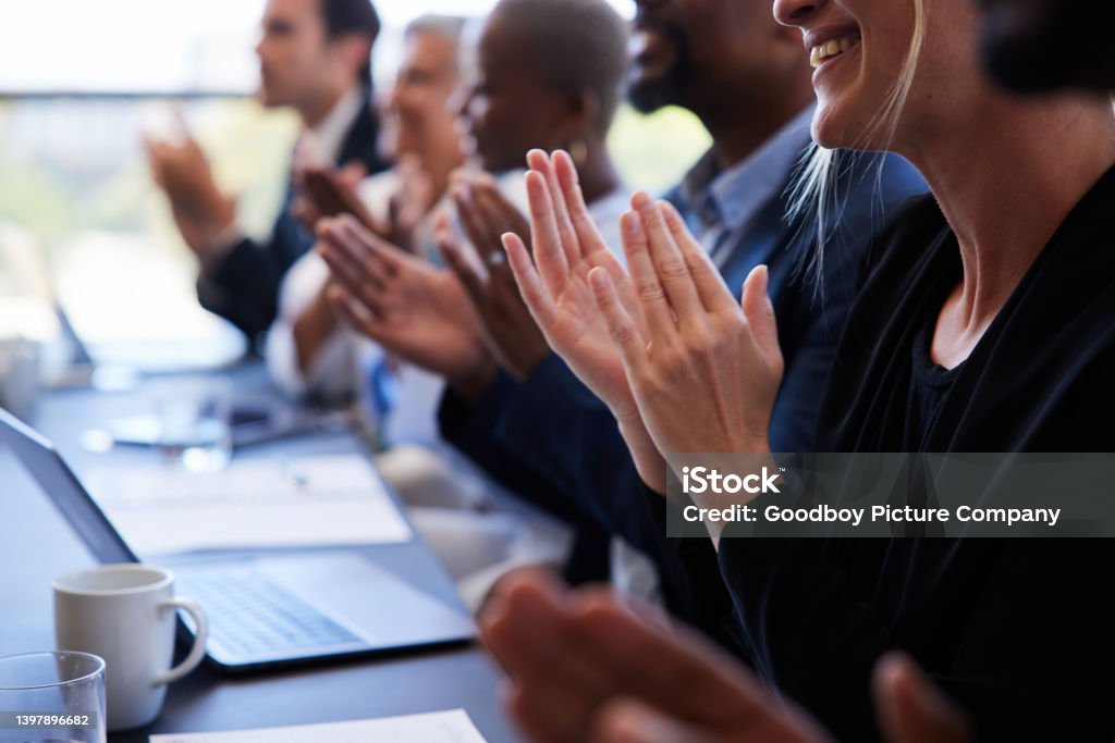 Diverse businesspeople sitting together at a boardroom table and clapping Close-up of a diverse group of smiling businesspeople sitting in a row at a table and clapping after a boardroom presentation Applauding Stock Photo