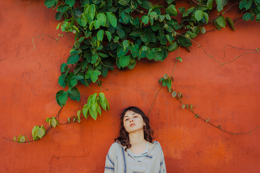 Young Caucasian woman standing  on the background of red wall and green plants