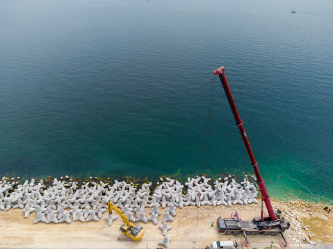 Aeria top view of breakwater construction. Bulldozer and crane on a pile of boulders in the sea