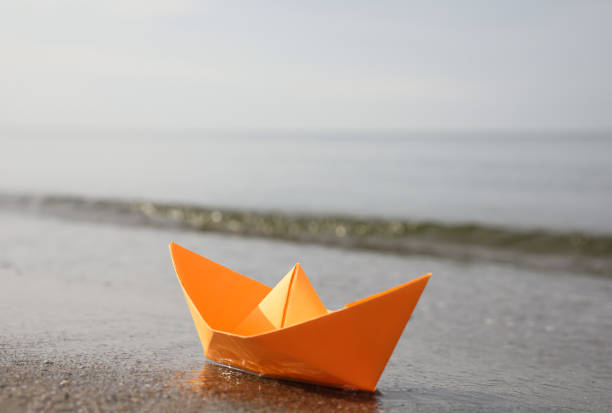 istock Orange paper boat on sandy beach near sea, space for text 1397902030