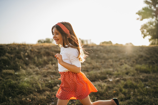 Cheerful girl running in green nature at summer sunset