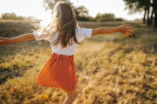 Back view of cheerful girl in red skirt running and spinning in  nature on sunny summer day