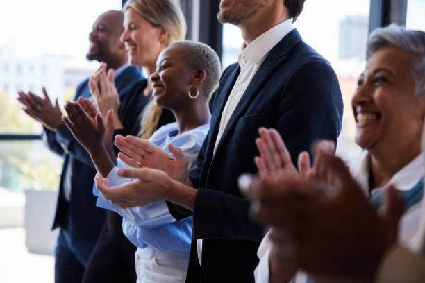 Diverse businesspeople smiling and clapping after a presentation in a boardroom Diverse group of smiling businesspeople standing together by windows in a boardroom and clapping after a presentation awards ceremony stock pictures, royalty-free photos & images