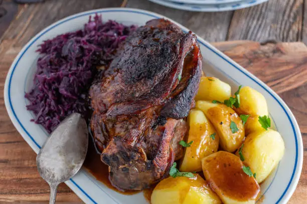 Delicious roast dish with oven roasted turkey shank, red cabbage, boiled potatoes and brown gravy. Served isolated on rustic and wooden table background from above
