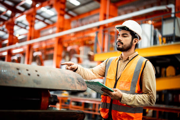 Men industrial engineer wearing a white helmet while standing in a heavy industrial factory behind. The Maintenance looking of working at industrial machinery and check security system setup in fact ingeniero industrial de hombres que lleva un casco blanco mientras está de pie en una fábrica industrial pesada detrás. el aspecto de mantenimiento de trabajar en maquinaria industrial y comprobar la configuración del sistema de seguridad de hecho