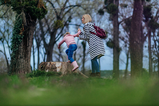 A stylish young mom with her daughter are playing in the park climbing on a tree stump