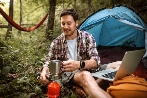 istock Young man working from his camp at forest, preparing coffee on a gas tank stove 1397915084